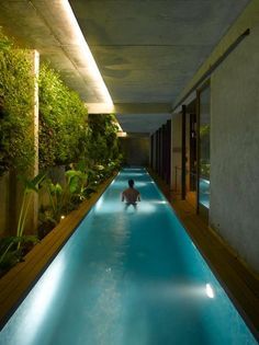 an indoor swimming pool in the middle of a building with plants on either side and people walking down it