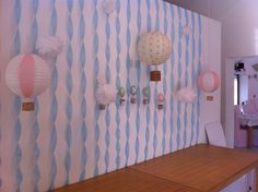 several paper lanterns are hanging on the wall above a table in a room with blue and white striped walls