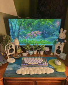 a computer desk with various items on it and a large screen in the back ground