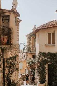 two people walking down an alley way in the middle of town with buildings on either side