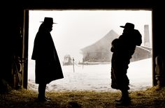 two people standing in front of an open barn door with snow falling on the ground