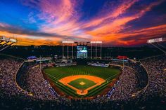 a baseball stadium filled with lots of people watching the sun go down over the field