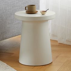 a white table with a cup and saucer on it next to a window in a living room