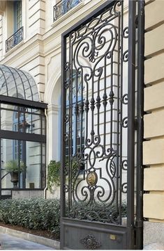 an ornate iron gate on the side of a building with glass doors and plants in front