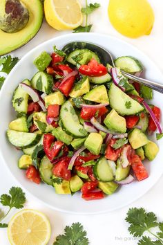 a white bowl filled with cucumber, tomatoes and onions next to sliced lemons