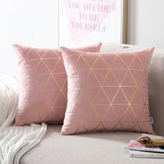 two pink and gold pillows sitting on top of a couch next to a white blanket