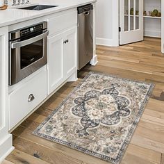 a kitchen with white cabinets and an area rug on the floor in front of the stove