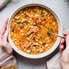 two hands holding a bowl of chicken and bean soup