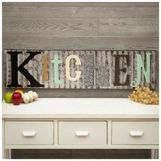 a kitchen sign sitting on top of a white table next to drawers and an apple