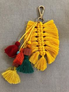 two tassels are attached to a keychain on a gray surface, one is yellow and the other is red