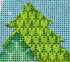 a cross - stitch christmas tree is shown on a piece of blue fabric with green leaves