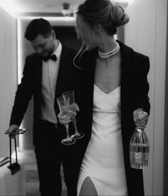 a man and woman are walking down the hallway with wine glasses in their hand,