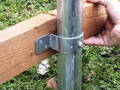 a person is holding onto a metal pole with wood in the background and grass on the ground