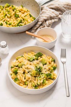 pasta with broccoli and cheese in a white bowl next to a glass of water