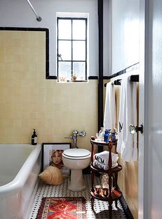 a white toilet sitting next to a bath tub under a window in a room with tiled floors