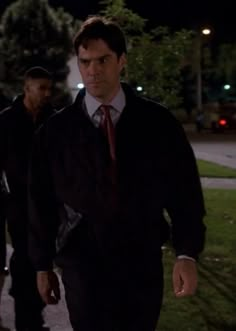 two men walking down the street at night with one man wearing a suit and tie