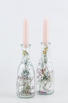 two glass bottles with flowers in them sitting next to each other on a white surface