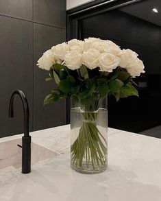 white roses in a clear vase on a marble countertop next to a black faucet