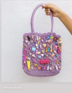 a hand holding a purple crocheted purse with lots of small items on it