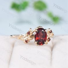 a ring with a red stone in the middle and two leaves on each side, sitting on top of a white cloth