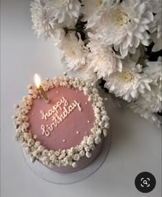 a pink birthday cake sitting next to white flowers