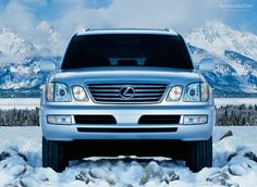 the front end of a silver suv parked on snow covered ground with mountains in the background