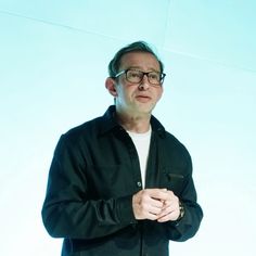 a man with glasses standing in front of a blue background