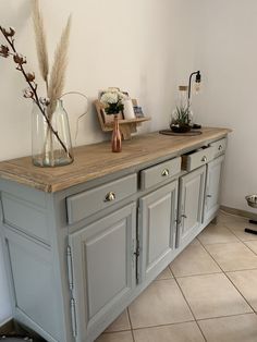 a large gray cabinet with two vases on top and flowers in the bottom drawer