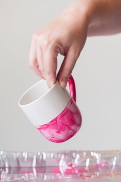 a person is holding a cup with pink paint on it and pouring water into it