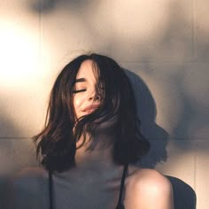 a woman with long hair wearing a black bra and posing in front of a white wall