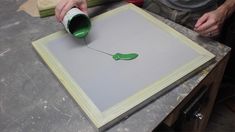 a person is painting on a piece of paper with a green paint roller in front of it