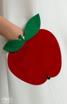 a woman's hand is holding an apple shaped piece of felt with green leaves on it