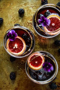 four glasses filled with blood orange punch and garnished with blackberries, on a table