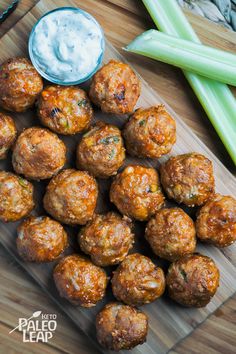 some meatballs are on a cutting board with celery sticks and a dip