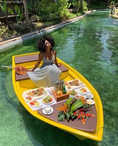 a woman sitting in a yellow boat with food on the bottom and water behind her