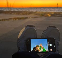 someone is taking a photo with their cell phone at sunset on the beach near the ocean