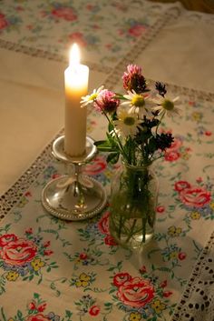 a vase with flowers and a lit candle on a doily covered tablecloth in front of a window