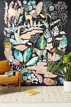 a living room with a couch, plant and wall mural