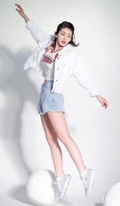 a woman in white shirt and jean shorts posing on top of a ball with her arms outstretched