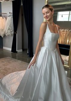 a woman standing in front of a mirror wearing a white dress and smiling at the camera