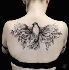 the back of a woman's shoulder with a bird and flowers tattoo on it