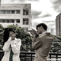 a man and woman standing next to each other in front of a tall building while talking on their cell phones