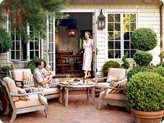 a patio with chairs, tables and potted plants in front of a house that has an open door