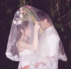 a bride and groom standing under a veil in front of some trees with flowers on it