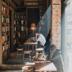 a man sitting at a table in front of a window next to a book shelf