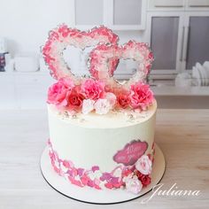 a decorated cake with pink flowers and two heart shaped letters sitting on top of it