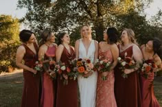 a group of women standing next to each other in front of trees and grass holding bouquets