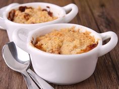 two white bowls filled with dessert sitting on top of a wooden table next to spoons