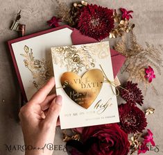 a person holding a heart shaped card in front of some red and gold paper flowers