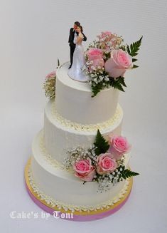 a wedding cake with pink flowers and a bride and groom figurine on top